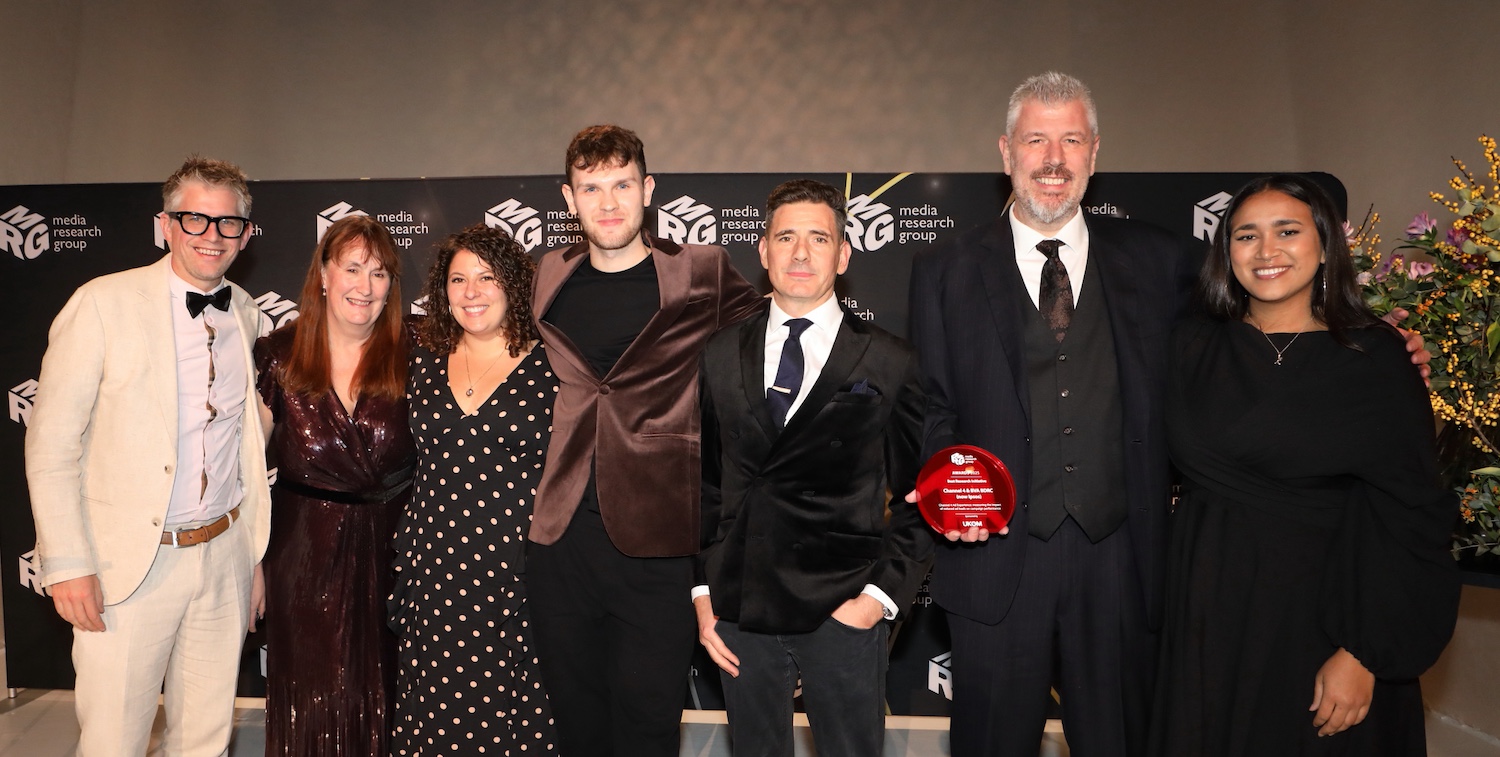 Seven individuals pose in front of the MRG Awards banner